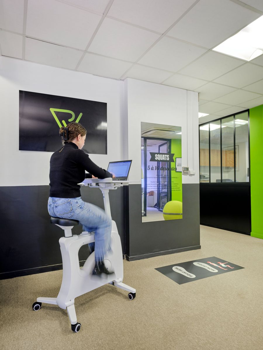 Collaboratrice travaillant sur un vélo de bureau, à côté de l'espace squats, chez Printvallée